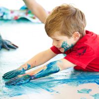 Kind malt mit blauer Farbe unter ganzem K&ouml;rpereinsatz